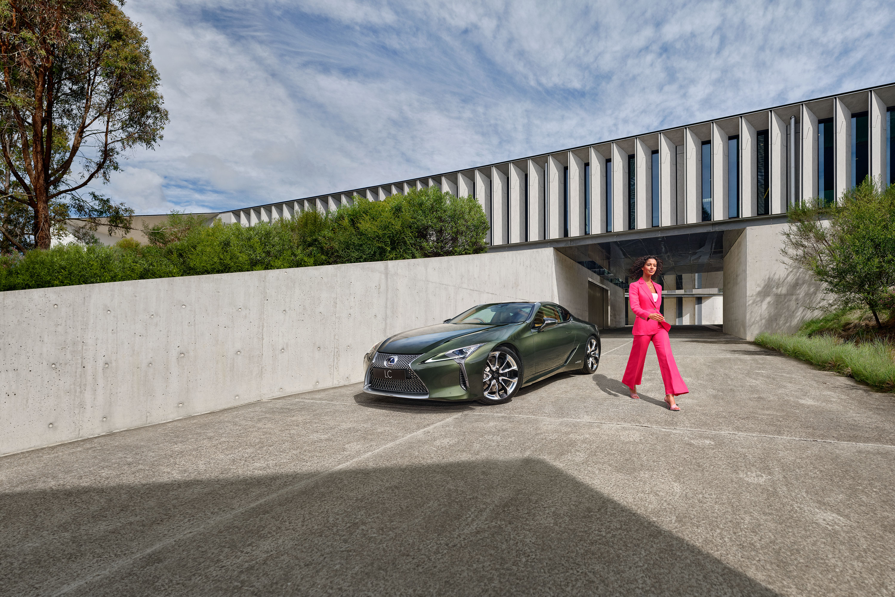 Woman dressed in a bright pink suit walks away from a Lexus LC coupe in Khaki Metal