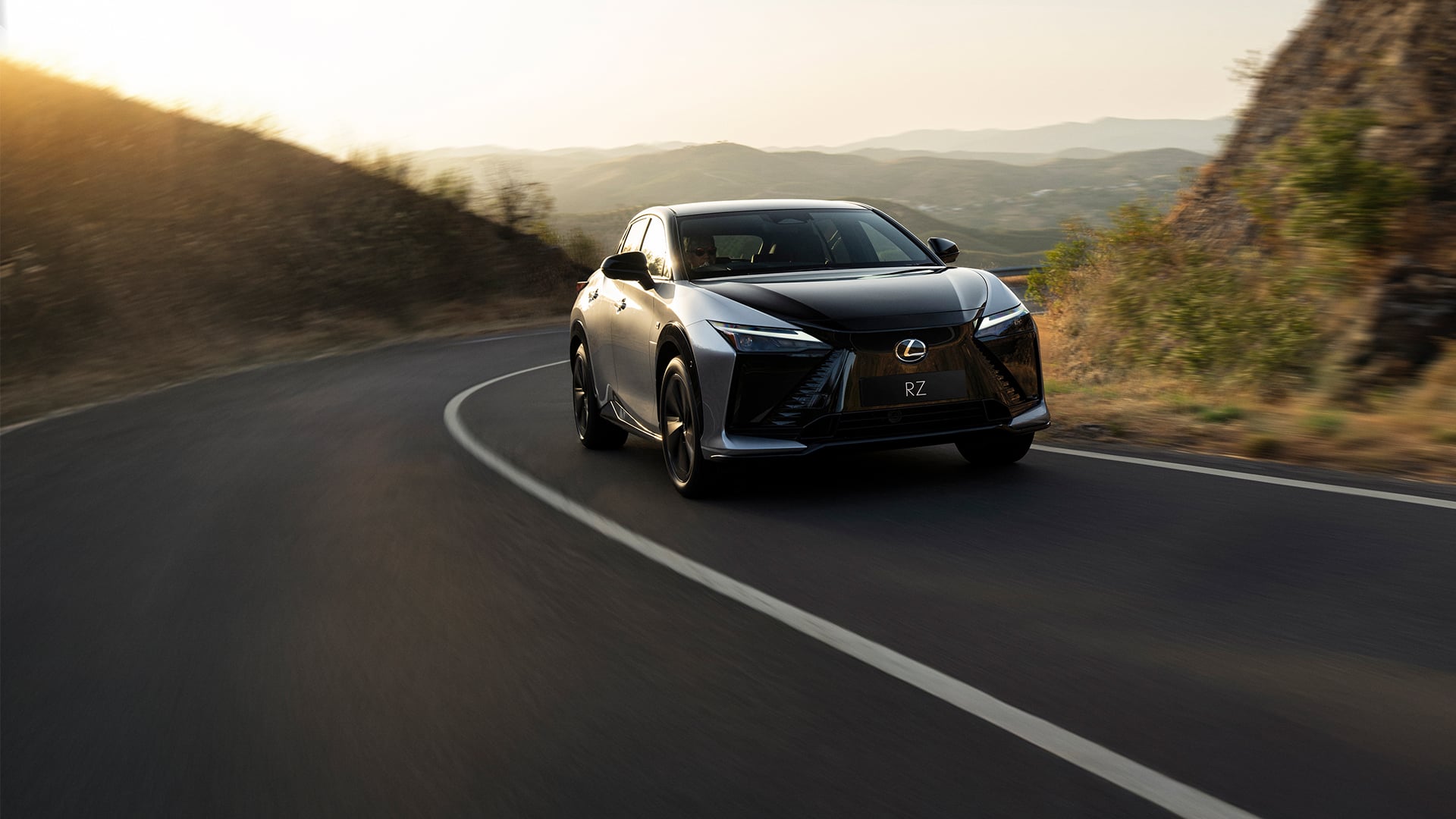 Lexus RZ driving along a road at sunset